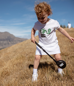 Child holding an adjustable golf driver, in a field of dry grass, with mountains in the background. Mini Hoshi branded golf club. 