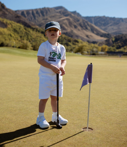 Child on a golf course with mountains in the background holding an adjustable golf putter