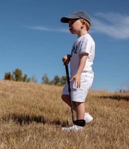 Child holding an adjustable golf wedge club, in a field with a clear blue sky.