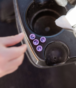 Close-up of a golf cart cup holder with the tops of purple golf tee's featuring an outline of a dog character on the heads. A small child's hand is blurred in the foreground reaching down to get one. Mini Hoshi branded golf tee's.