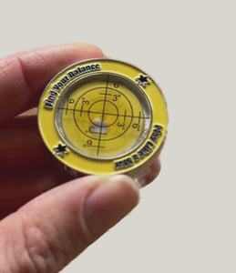 Video of a hand up close holding a yellow ball marker and turning it over to revel a level at the back of the golf ball maker. Test ' Find your Balance' and 'Play like a star' can be read on the outside edges. 
